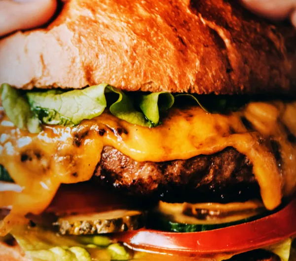 Close up of burger with cheese, pickles, tomato and lettuce.