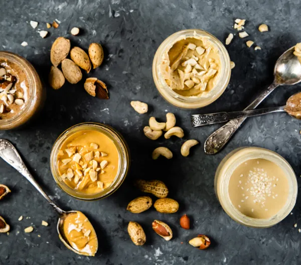 overhead shot of jars of different nut and seed butters with spoons on grey background
