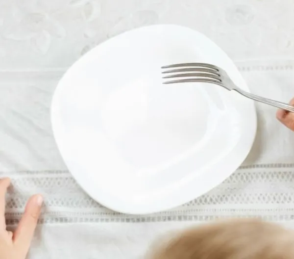 A child holds a fork over an empty plate