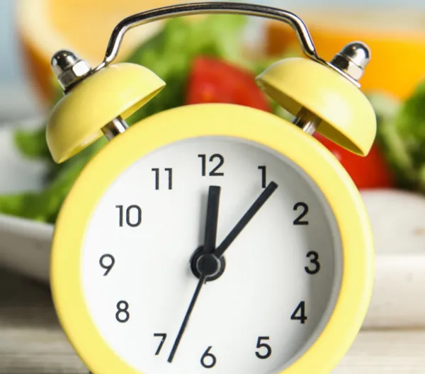 old yellow alarm clock in front of a plate of salad