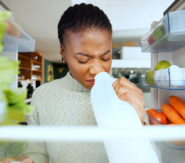 woman sniffing milk carton inside a fridge