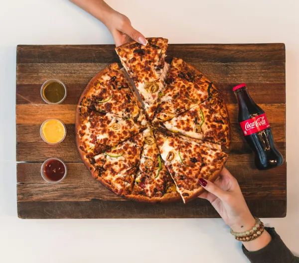 Overhead view of a pizza and bottle of soda on a cutting board