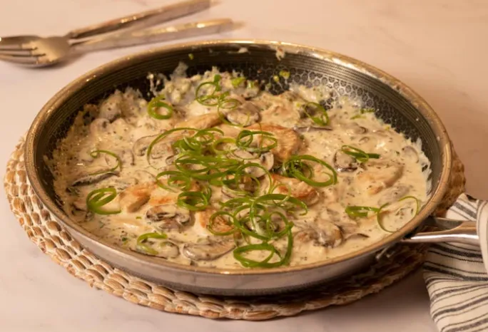 large pan filled with chicken, mushrooms, creamy sauce and topped with green scallion strips
