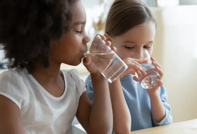 2 young girls drinking water out of clear glasses