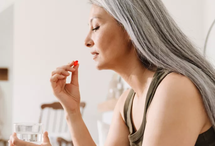 woman holding a glass of water and red supplement close to her mouth