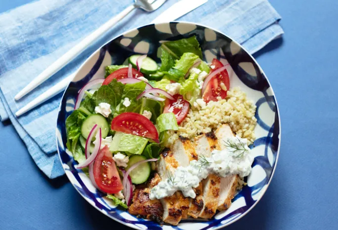 bowl on a blue background with greens and chicken