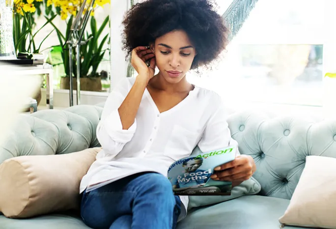 woman sitting on a couch and reading a Nutrition Action magazine