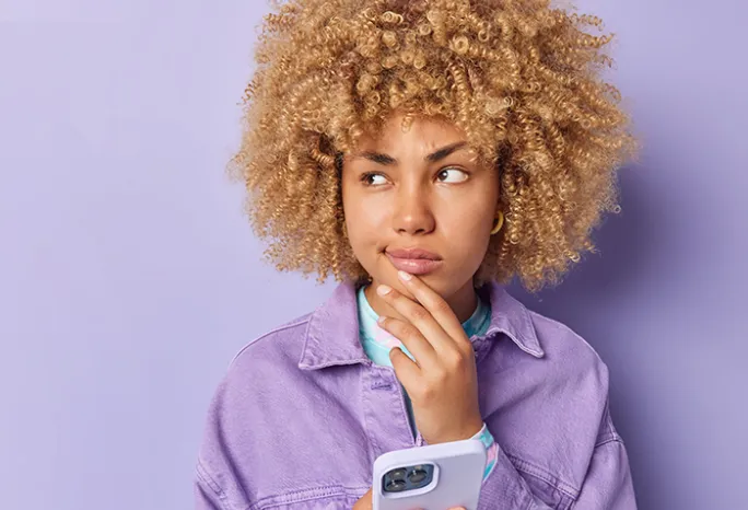 person in purple shirt with purple background holding a phone and holding their chin