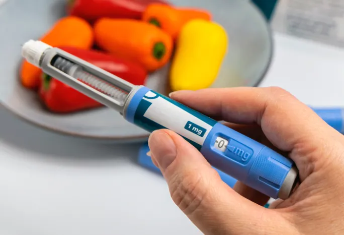 hand holding an obesity medication applicator with bell peppers in the background