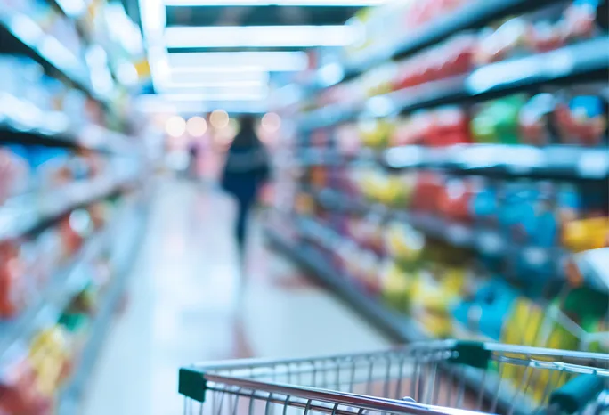 grocery cart in focus in the foreground with grocery store shelves out of focus in the background