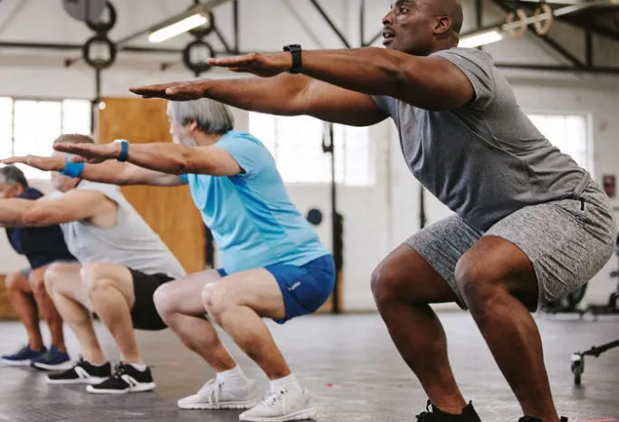 4 older men holding a squat in the gym