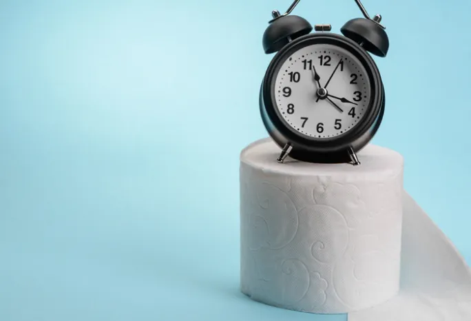 alarm clock sitting on a roll of toilet papper