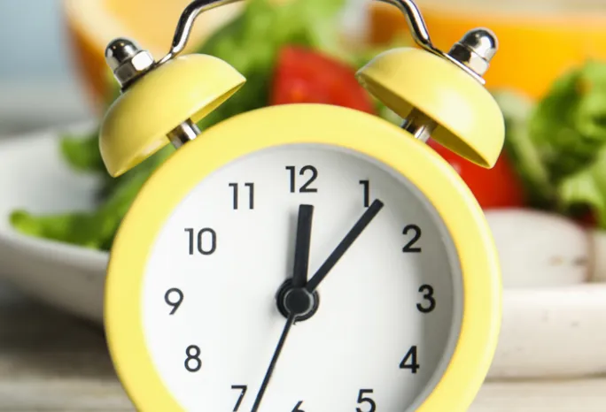 old yellow alarm clock in front of a plate of salad