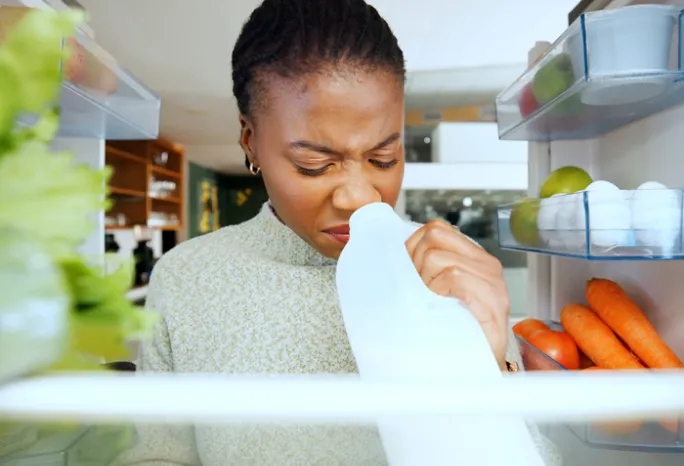 woman sniffing milk carton inside a fridge