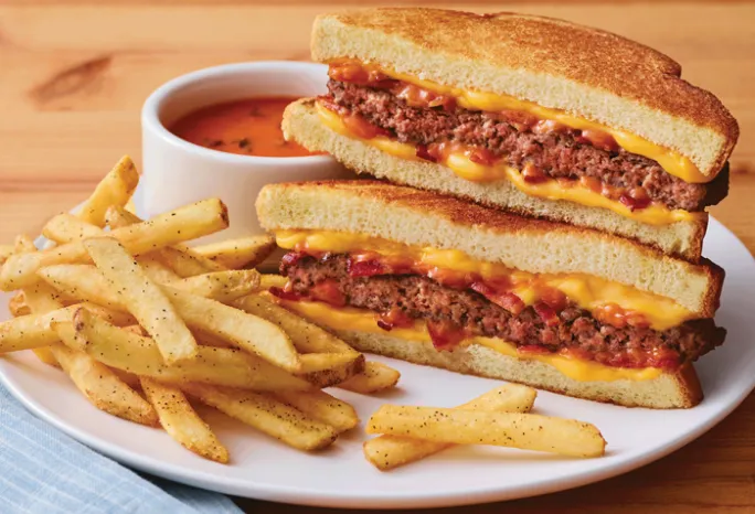 cheeseburger grilled cheese on a plate with fries and small bowl of tomato soup.