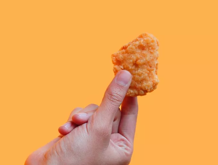 A hand holding a chicken nugget