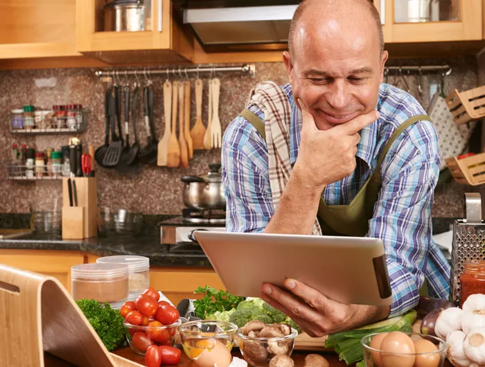 man in kitchen looking at ipad with lots of vegetables on the counter