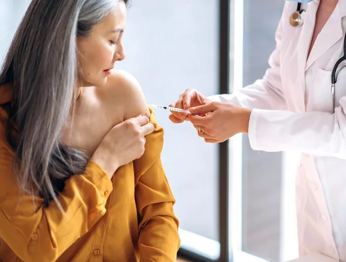 women in yellow top receiving a vaccine from the doctor