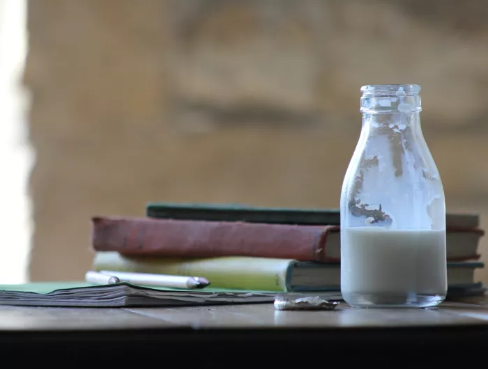 Half full container of plain milk next to books and pencils