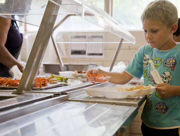 A boy in the school cafeteria adding foods his lunch tray