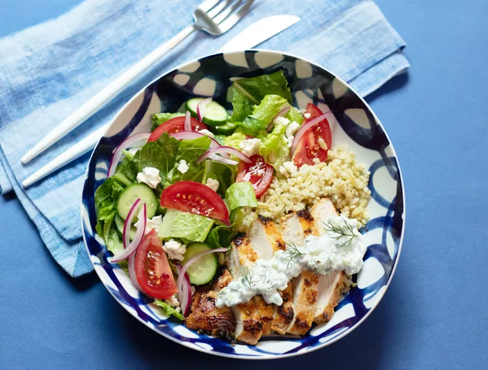 bowl on a blue background with greens and chicken