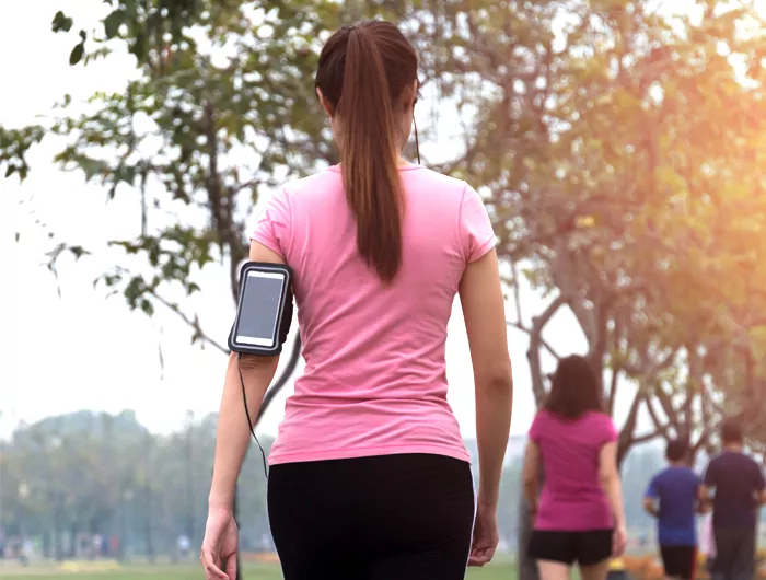 woman in a pink shirt walking away from the camera and waring a phone holder on her arm