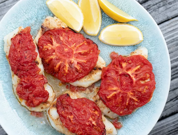 Plate of white fish with tomatoes on top