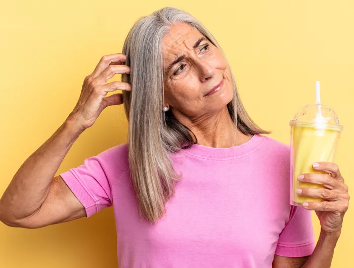 Older woman scratching her head and holding a yellow shake
