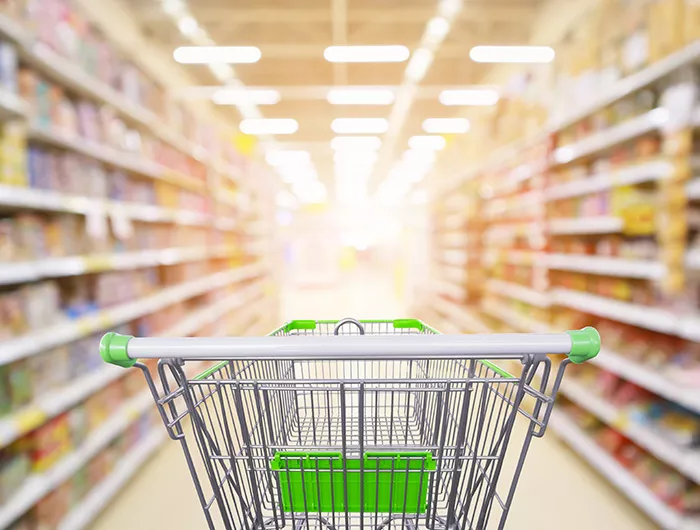 Supermarket aisle product shelves interior blur background with empty shopping cart