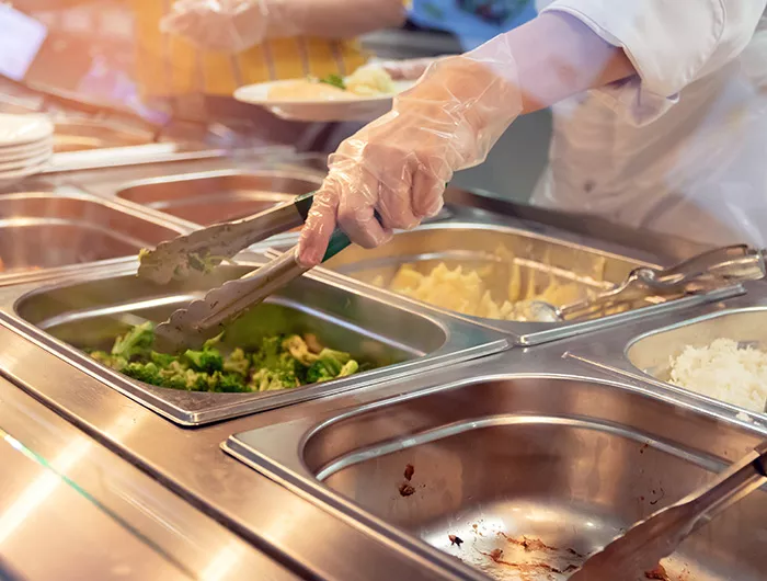 Chef standing behind full lunch service station with assortment of food in trays.