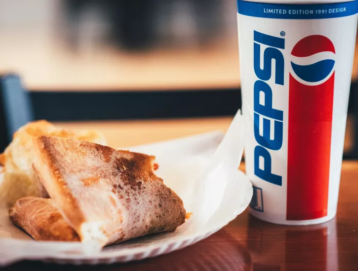 A slice of pizza on a paper plate and a fountain soda in a Pepsi cup