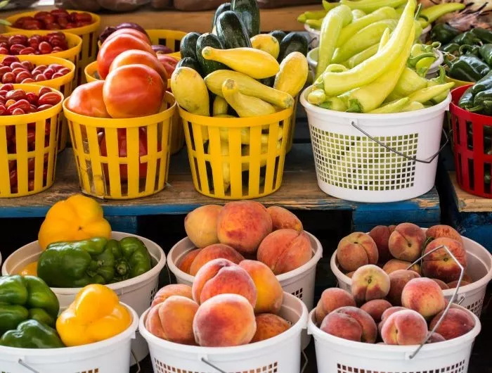 Seasonal produce - baskets of tomatoes, squash, peppers, peaches and other fruit and vegetables for sale in July
