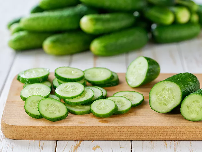 Whole and sliced fresh cucumbers on a cutting board on a wooden table