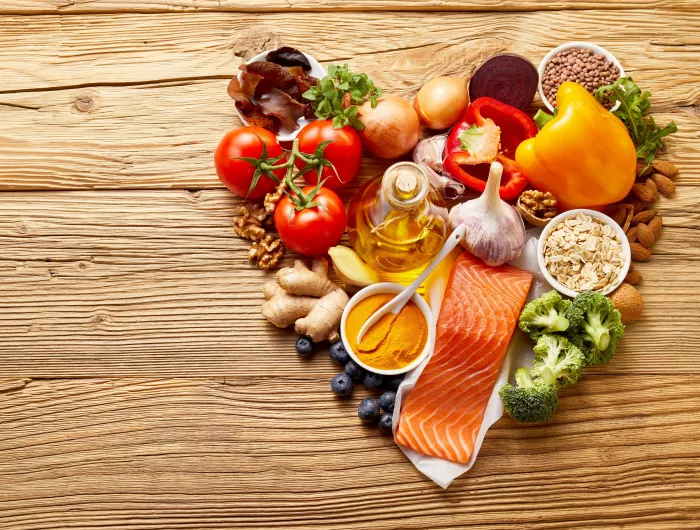 A collection of food in the shape of a heart including raw salmon, olive oil, ginger, nuts, berries, oats, beans, and assorted fruits and vegetables.