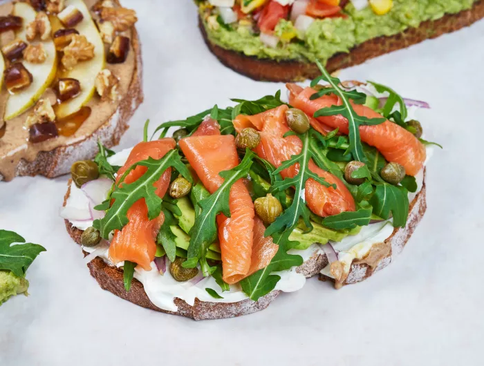 Slices of toast topped with salmon, nuts, and avocado, respectively.