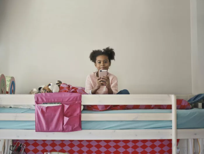 A young girl sitting on her bed holding an iphone.