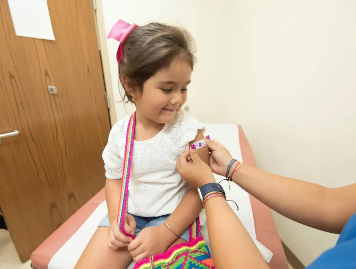 A young girl smiles as a nurse puts a colorful bandage on her arm after administering a vaccine.
