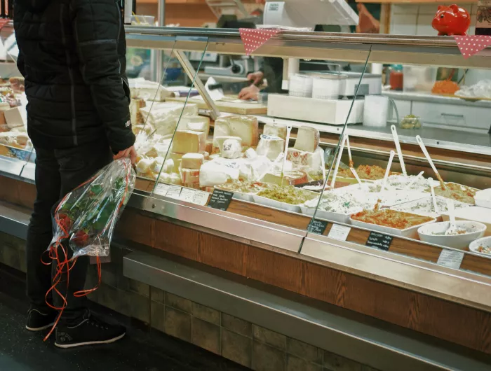 A man with flowers standing in front of a deli display containing various salads
