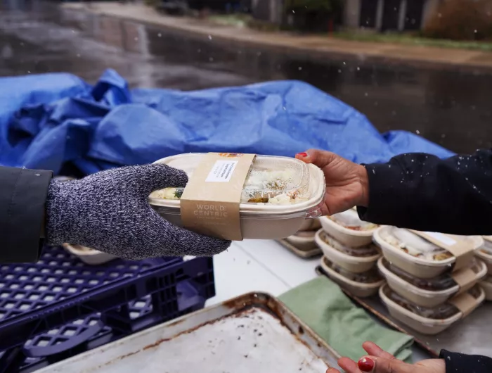 A Make Food Not Waste worker hands a recipient a meal