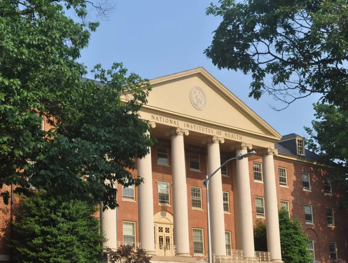 James H. Shannon Building (Building One), NIH campus, Bethesda, MD. A brick Georgian Revival building flanked by trees under a blue sky.