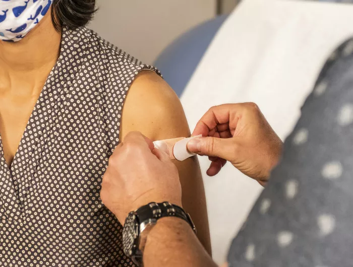 A band-aid being placed on a woman's arm after receiving a vaccine.