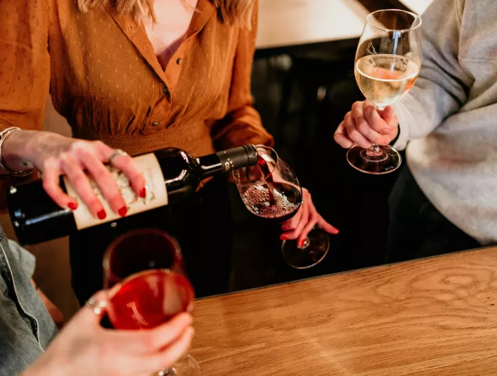 A seated woman pouring herself a glass of red wine.