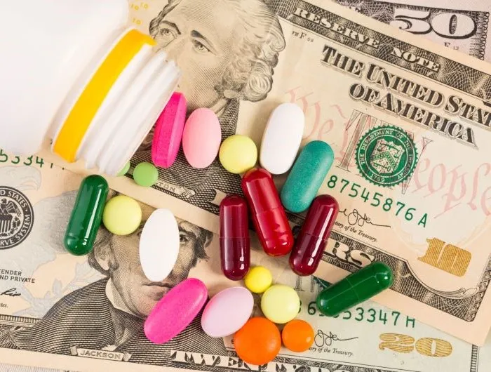 Money with a handful of supplements and tablets on top.