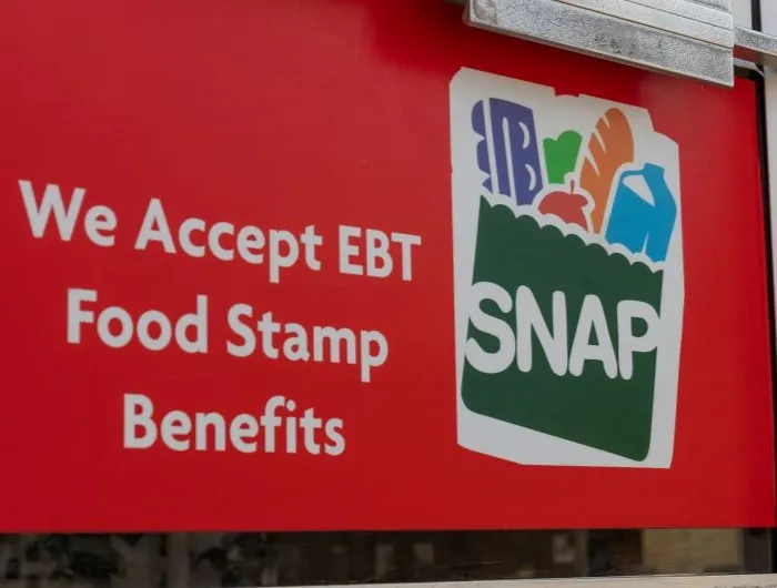 A store window displays a red sign that reads "We accept EBT Food Stamp benefits" with the SNAP grocery logo.
