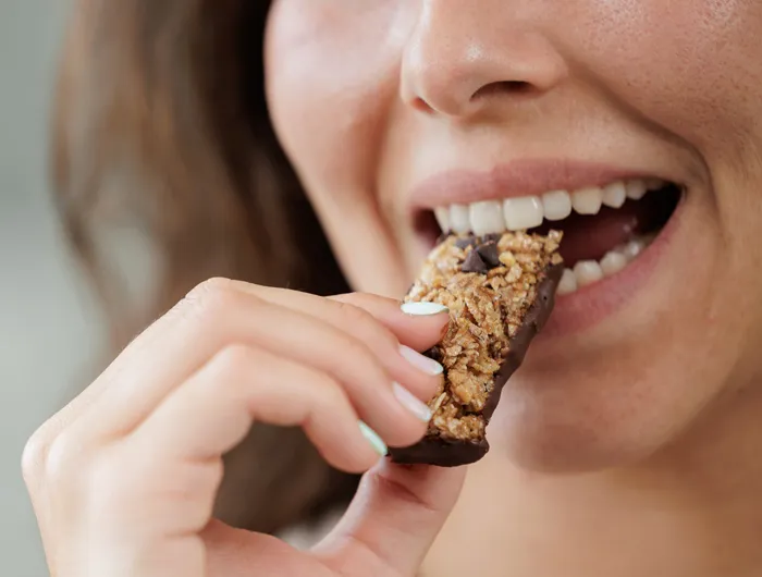 woman taking a bite of granola or protein bar
