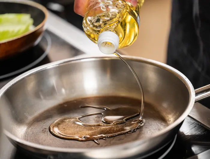 oil being pored from bottle into stainless steal pan