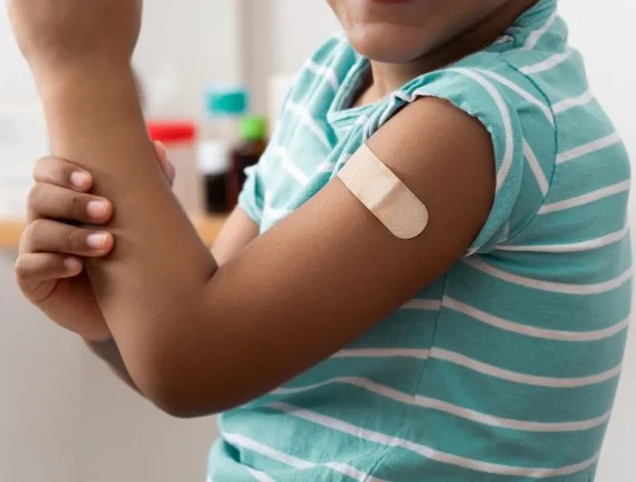 A Black child shows off their arm with a bandage over a vaccine injection site