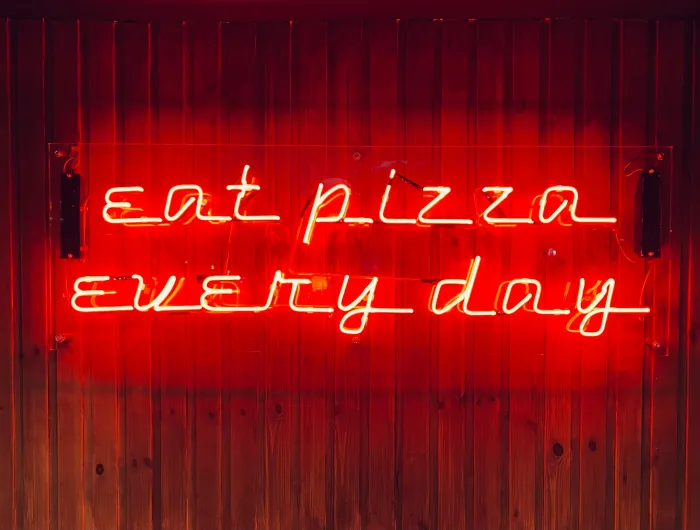 A red neon sign reading "eat pizza every day"