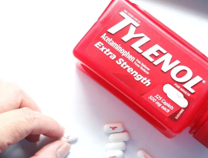 A hand picks up a tablet of Tylenol from a white surface beside a red bottle of Tylenol Extra Strength acetaminophen, which RFK and Trump wrongly assert causes autism.