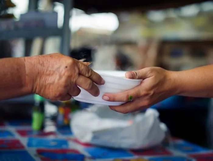 Closeup of a person handing a bowl of food to another person.